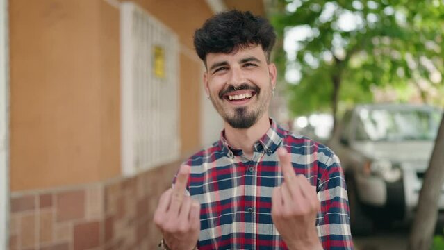 Young hispanic man smiling confident doing bad gesture with fingers at street