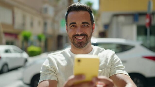 Young hispanic man smiling confident making photo by the smartphone at street