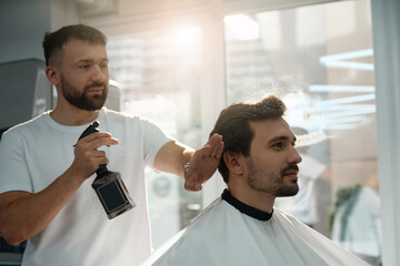 Qualified barber applying spray to client hair