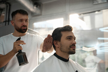 Professional barber moisturizing his client hair before trimming it