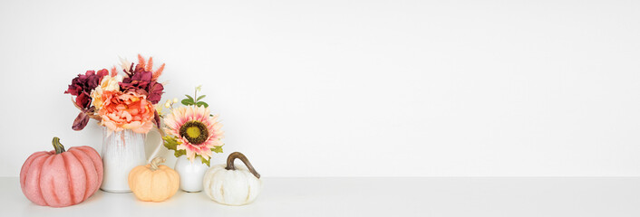 Fototapeta Autumn decor on a white shelf against a white wall banner background. Pumpkins and flowers in vases with pink hue fall colors. Copy space. obraz
