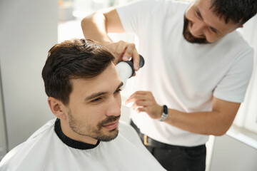 Fototapeta premium Cheerful hairstyle specialist brushing guest face after cutting hair