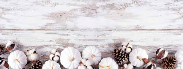 Autumn bottom border of white pumpkins and brown fall decor. Top view on a white wood background with copy space.