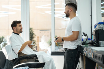 Contented handsome man enjoying coffee and service in hair salon