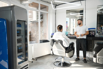 Pleasant hair salon worker entertaining his guest with conversation