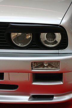 Round twin front headlights of first generation of high performance compact coupe BMW E30 M3 with tuning black upper headlight cover. Displayed on car expo in Bratislava, Slovakia.