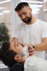 Obraz na płótnie Canvas Young brunet man having his face shaved at hair salon
