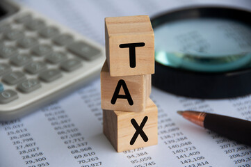 Tax word on wooden blocks with calculator, pen, magnifying glass and data analysis background. Tax concept