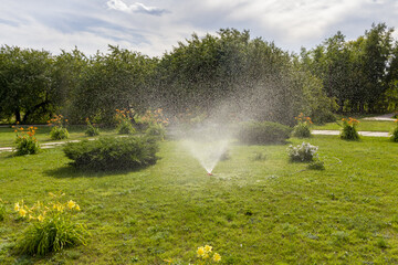 Fountain of the automatic garden irrigation system in the rays of the midday sun.