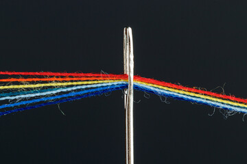 multi-colored threads for sewing in the form of a rainbow pass through an antique needle on a black background