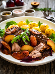 Roast pork loin with plums and fried potatoes on wooden table
