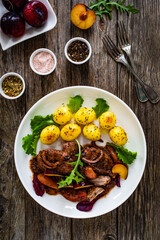 Roast pork loin with plums and fried potatoes on wooden table

