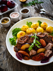 Roast pork loin with plums and fried potatoes on wooden table
