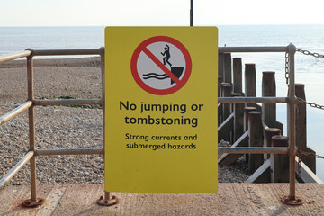 A yellow sign by the sea prohibiting jumping or tombstoning due to strong currents and submerged...