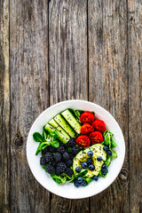 Fresh salad - avocado, blackberries, cucumber, cherry tomatoes, blueberries and greens on wooden table
