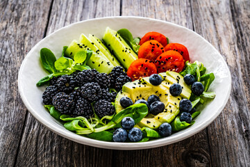 Fresh salad - avocado, blackberries, cucumber, cherry tomatoes, blueberries and greens on wooden table
