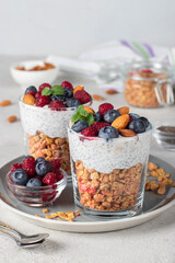 Chia seeds pudding with muesli, fresh berries and almonds in glasses on gray plate. Healthy breakfast concept