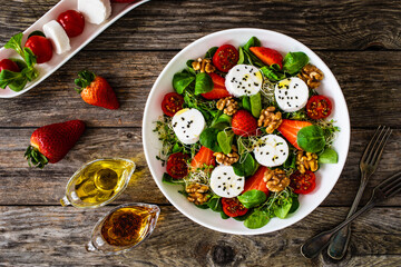 Fresh salad - goat cheese, strawberries, walnuts, cherry tomatoes and leafy greens on wooden table
