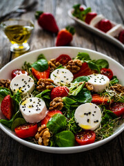 Fresh salad - goat cheese, strawberries, walnuts, cherry tomatoes and leafy greens on wooden table

