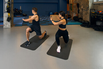 Sportive couple practicing crescent lunge on the yoga mat at the gym