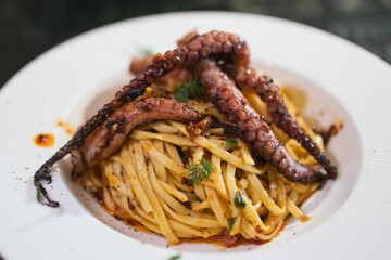 Close up of the spicy grilled squid pasta aglio olio on white plate with black wooden table