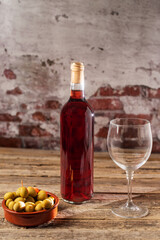 Bottle of rosé wine next to a glass and a plate with olives. Close-up.