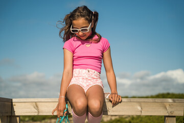 Child girl in vivid outfit sitting at the wooden bridge and enjoying of the summer