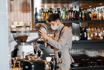 A masked barista prepares an exquisite delicious coffee at the bar in a coffee shop. The work of restaurants and cafes during the pandemic.