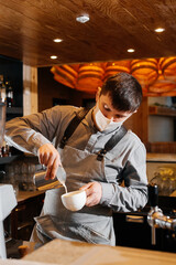A masked barista prepares an exquisite delicious coffee at the bar in a coffee shop. The work of restaurants and cafes during the pandemic.