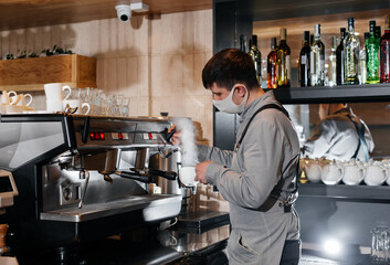 A masked barista prepares an exquisite delicious coffee at the bar in a coffee shop. The work of restaurants and cafes during the pandemic.
