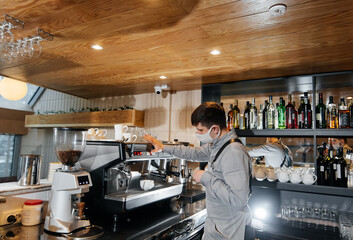 A masked barista prepares an exquisite delicious coffee at the bar in a coffee shop. The work of restaurants and cafes during the pandemic.