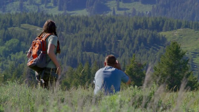 Lovely couple of tourists hiking along wild trails of the Grand Teton National Park. Back view of a man in blue t-shirt taking pictures of pristine backcountry landscape. High quality 4k footage