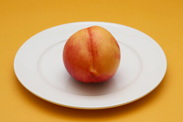 Nectarine in a white plate on an orange background. Shallow depth of field