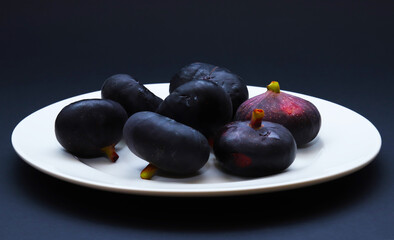 Dark figs in a white plate on a dark background. Shallow depth of field