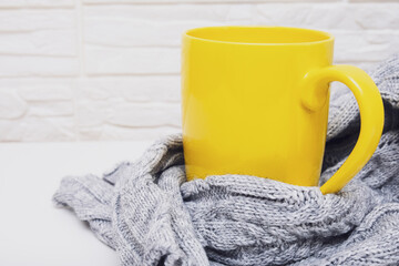 Autumn mood. Yellow cup of hot tea or coffee with a cosy knitted sweater against white backdrop with copy space