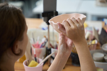 Woman holds blank clay plate in front of her eyes