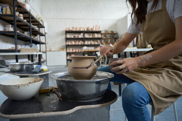 Master woman sits at potter wheel and decorates clay vase