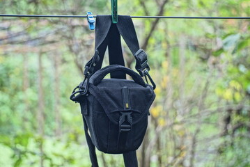 one black bag made of fabric hangs on a harness on a wire among green vegetation on the street