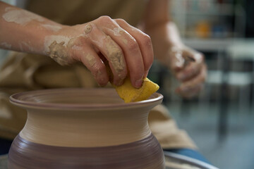 Potter with sponge polishes edges of vase on potter wheel