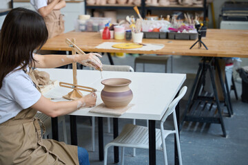 Woman sits at a worker and decorates a clay vase