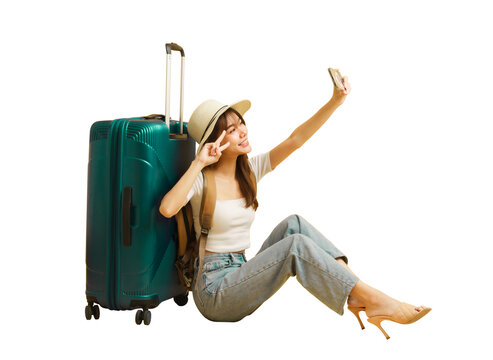 Asian beautiful woman traveler sitting nearby luggage and raised smartphone to selfies.