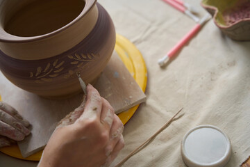 Craftswoman sits at table and works with loop on vase