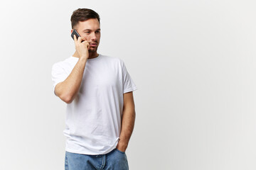 Happy passionate tanned handsome man in basic t-shirt talk with business partner using phone posing isolated on white studio background. Copy space Banner Mockup. Distance online communication concept