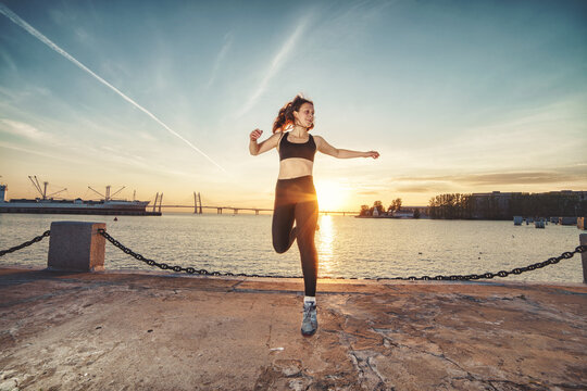 Young happy athletic looking woman jumping up against sea and sunset sky