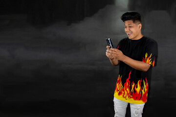 Man with polo shirt with flames holds a smart cell phone. Technology concept on black gradient...
