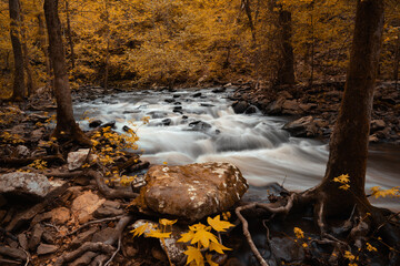 A river stream cascades over mountain rocks during fall in the Ozark Mountains.