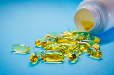 Fish oil capsules with omega 3 and vitamin D with bottle, isolated on blue background. Yellow vitamin pills. Medicine and healthy.