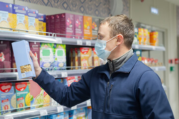 A man in a protective face mask chooses products in the store. Groceries. Food and drinks