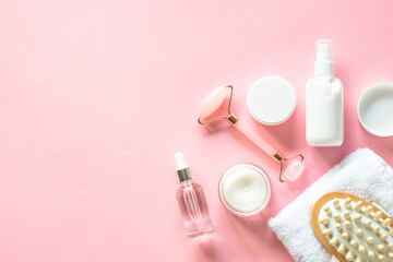 Natural cosmetics on pink. Skin care product, cream, soap serum, jade roller and white towel. Flat...