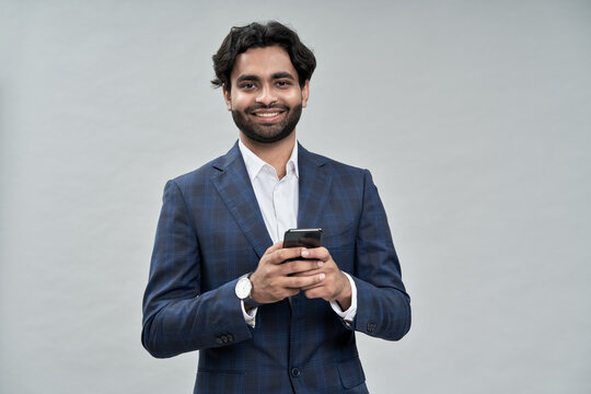 Smiling Young Successful Rich Arab Indian Professional Business Man Wearing Suit Holding Smartphone Using Cell Mobile Phone Isolated On Beige Background Advertising Corporate Online Applications.